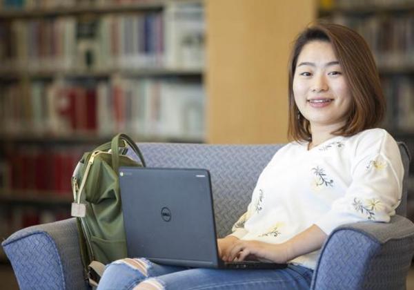 Smiling female student in a library sitting with a laptop on her lap