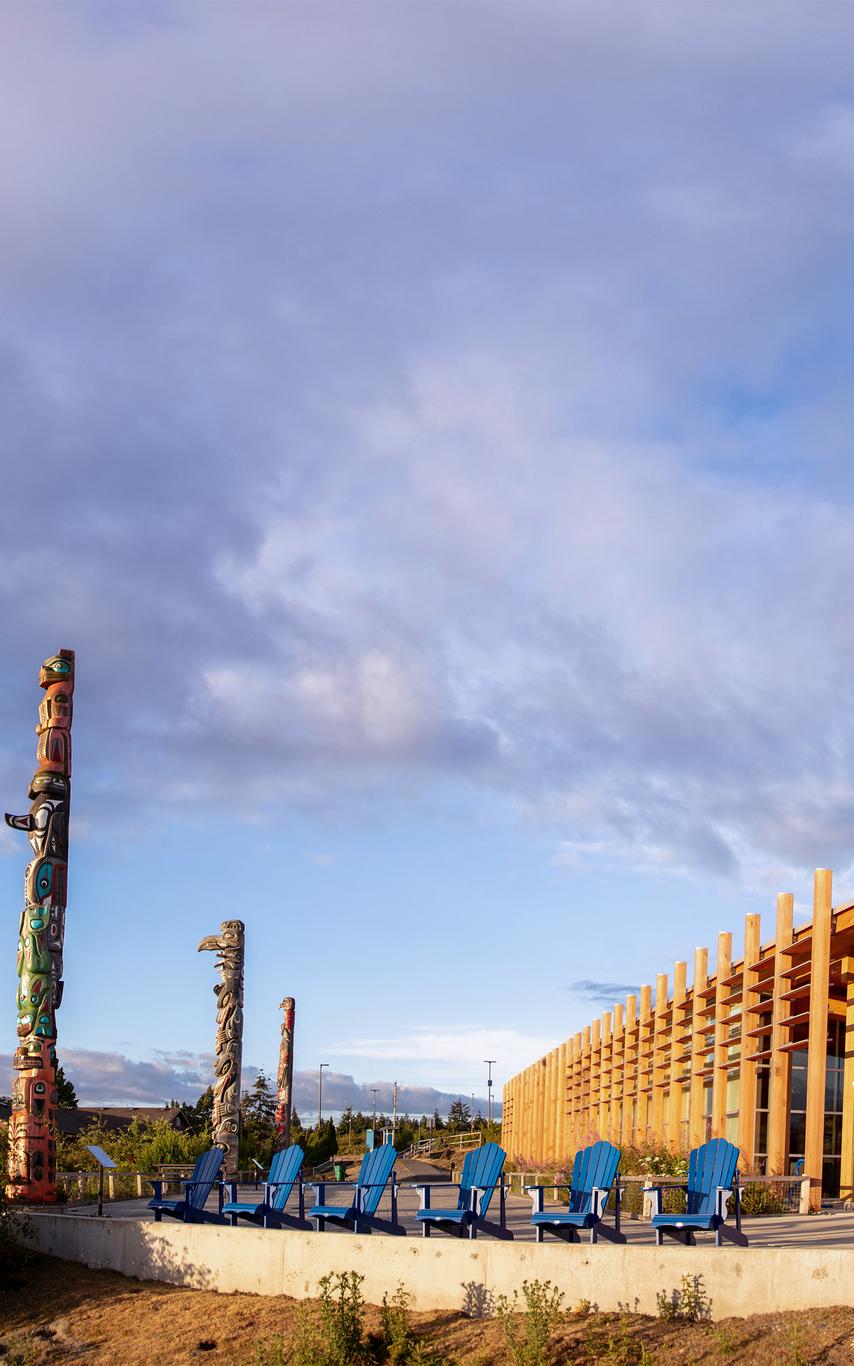 Modern wood building with three totem poles outside. 